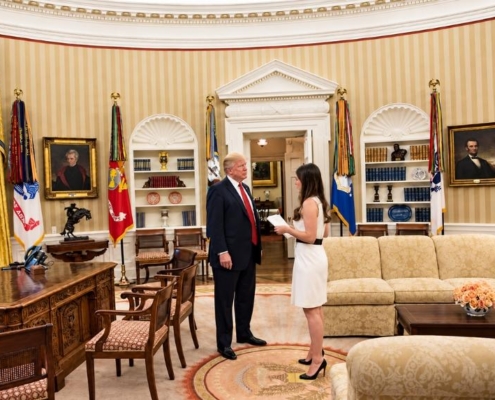 U.S. president speaking with a woman holding documents during a meeting in the White House.